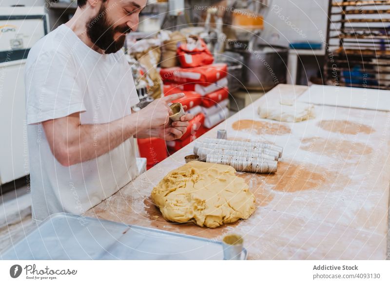 Bärtiger Konditor legt Teig in Tasse Bäckerei Teigwaren setzen Tisch Küche Gebäck Vorbereitung frisch Mann roh professionell Lebensmittel Küchenchef Restaurant