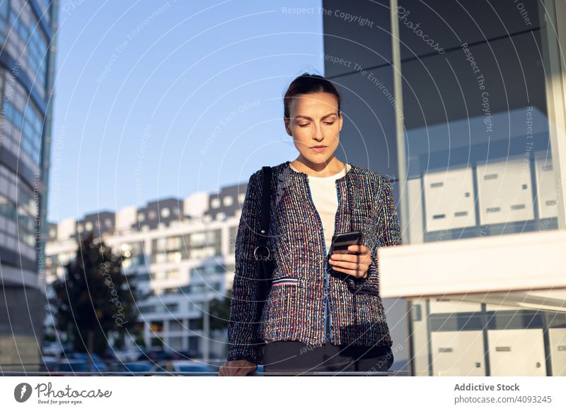 Lächelnde Geschäftsfrau beim Telefonieren mit dem Handy Smartphone Gebäude Büro Eingang Straße modern Großstadt urban Frau heiter Arbeit Wand Glas Job Mobile