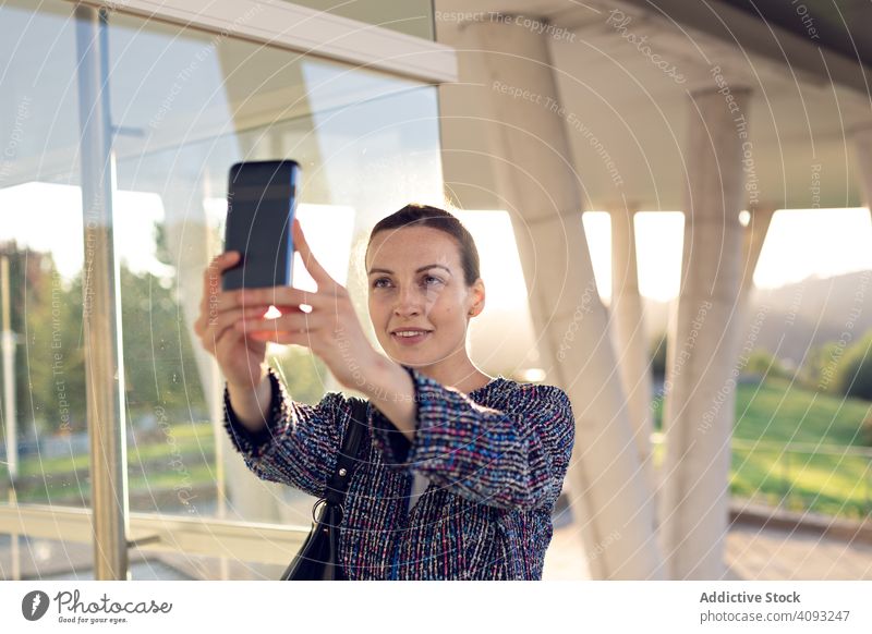 Lächelnde Geschäftsfrau nimmt Selfie auf der Straße Smartphone Gebäude Büro Eingang modern Großstadt urban Frau heiter Arbeit Wand Glas Job Telefon Mobile Gerät