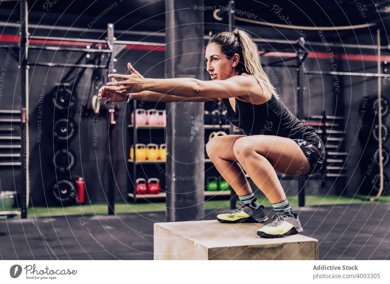 Sportliche Frau springt auf einen Kasten, um ihre Ausdauer im Fitnessstudio zu verbessern Trainerin Training muskulös springend Übung sportlich Klient