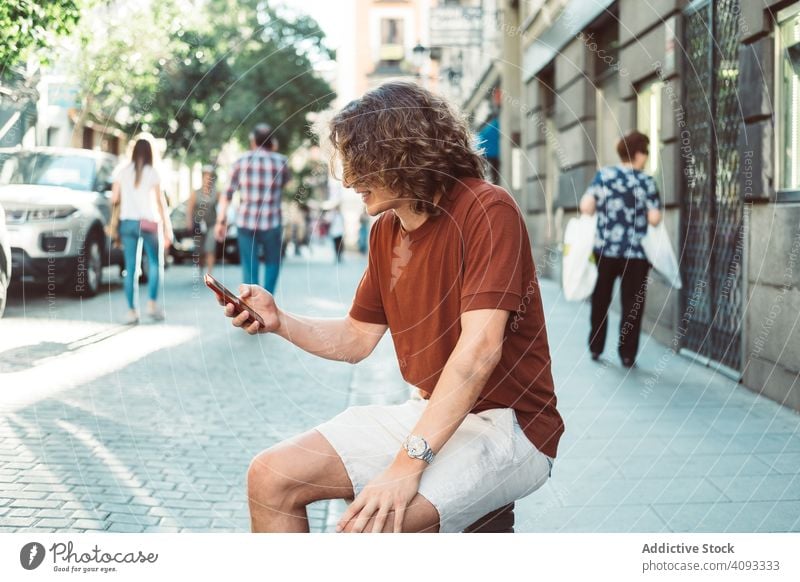 Amüsierter Mann mit Longboard, der sich auf der Straße ausruht und telefoniert reden Telefon amüsiert lässig Lachen gestikulieren heiter benutzend sprechen