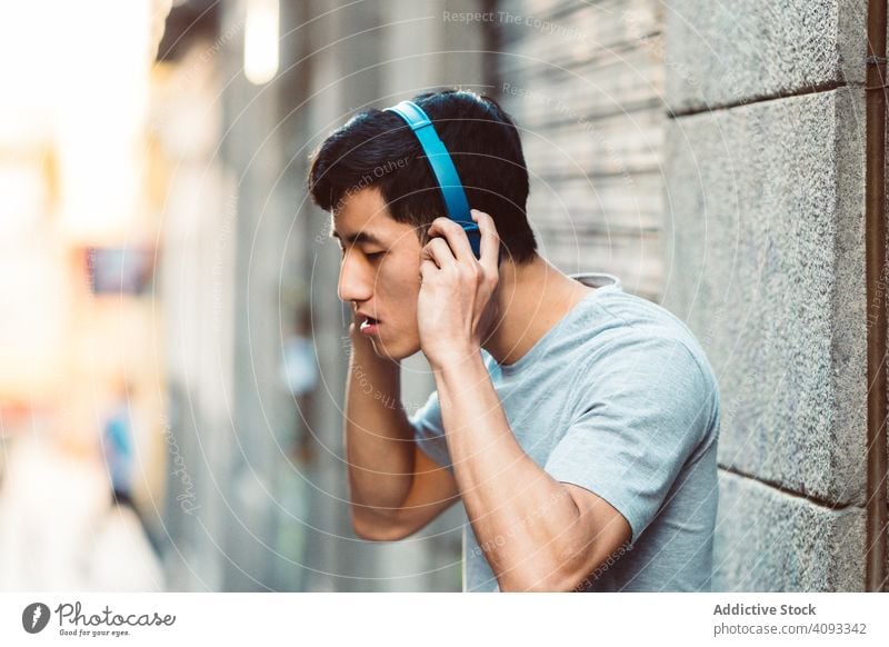 Mann mit Kopfhörern, der auf der Straße Musik hört Großstadt zuhören benutzend Streaming Inhalt cool freudig modern lässig stehen sonnig Stadt jung Erwachsener