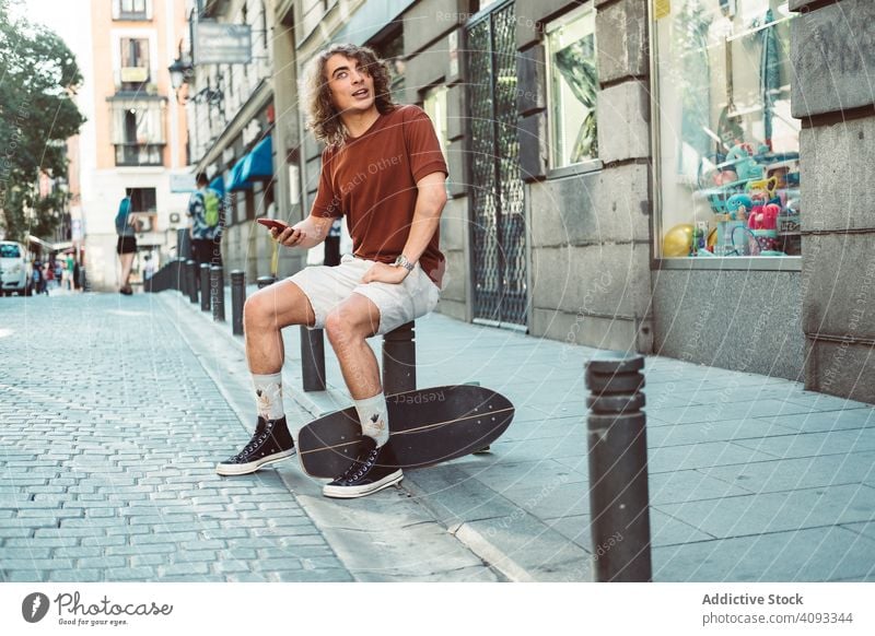 Amüsierter Mann mit Longboard, der sich auf der Straße ausruht und telefoniert reden Telefon amüsiert lässig Lachen gestikulieren heiter benutzend sprechen