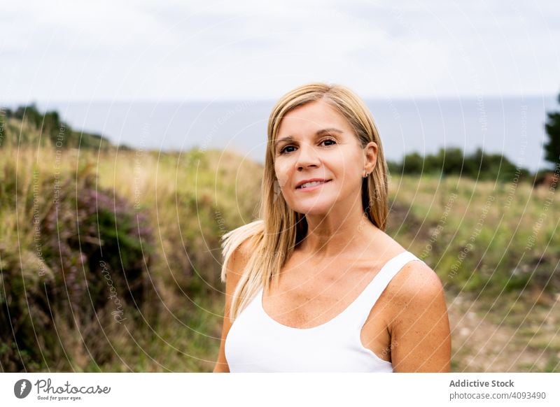 Charmante Frau schaut in die Kamera, während sie auf dem Land spazieren geht Landschaft Feld genießend Wald friedlich Lächeln Natur grün Erholung lässig