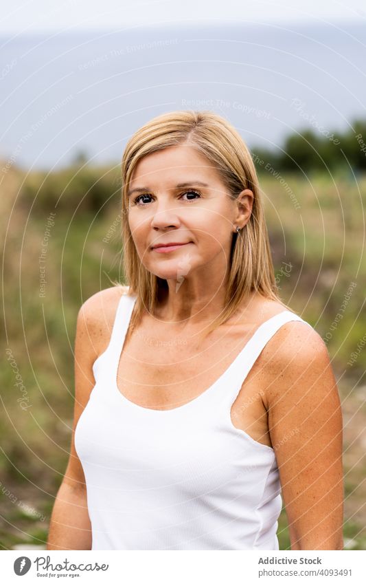 Charmante Frau schaut in die Kamera, während sie auf dem Land spazieren geht Landschaft Feld genießend Wald friedlich Lächeln Natur grün Erholung lässig