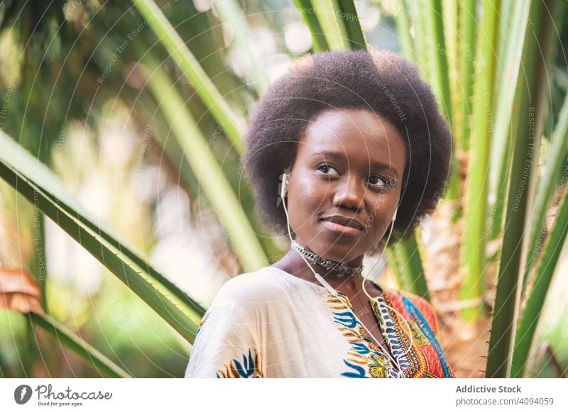 Lächelnde schwarze Frau beim Hören von Musik zuhören Kopfhörer Afrikanisch Handfläche traditionell farbenfroh Freude ethnisch heiter Glück Melodie Audio Gesang