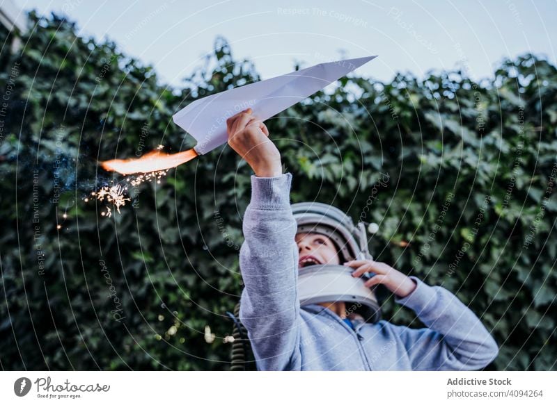 Überraschtes Kind hat Spaß mit funkelndem Flugzeug Junge spielen Ebene Spielzeug aufgeregt Papier petard überrascht Astronaut Schutzhelm Garten Glück Kindheit