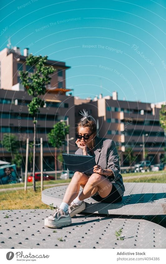 Stilvolle Frau sitzt und blättert auf einem Tablet im Freien Geschäftsfrau Tablette Straße Großstadt Business urban Dame Internet benutzend digital Mitteilung