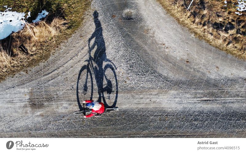 Luftaufnahme mit einer Drohne von einer Fahrradfahrerin auf einer Straße mit Schatten luftaufnahme drohnenfoto frühling sport radfahren fahrrad frau