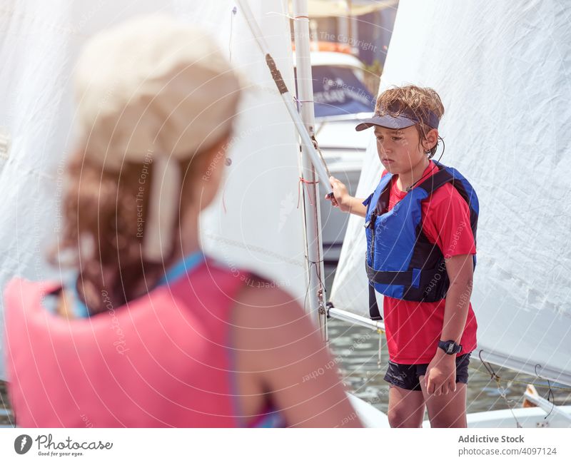 Junge in blauer Schwimmweste auf Jacht Schwimmsport kreuzend Wasser Sicherheit Ufer Wellen Meer Badebekleidung Kind gespannt Training Gesundheit Lernen