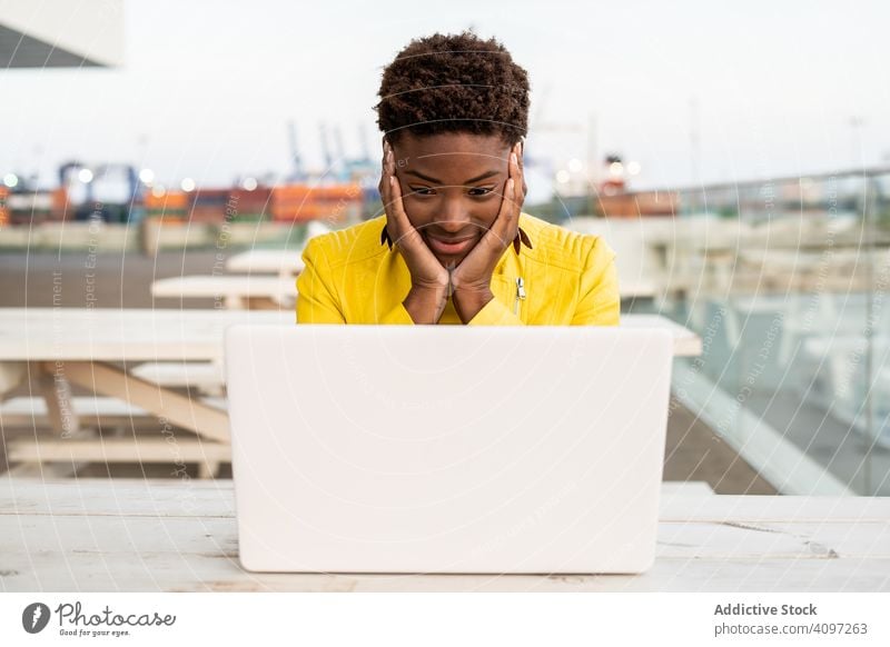 Frau arbeitet am Laptop am Tisch benutzend Arbeit Schreibtisch Großstadt Afroamerikaner Jacke gelb hölzern jung lässig Arbeitsplatz beschäftigt abgelegen