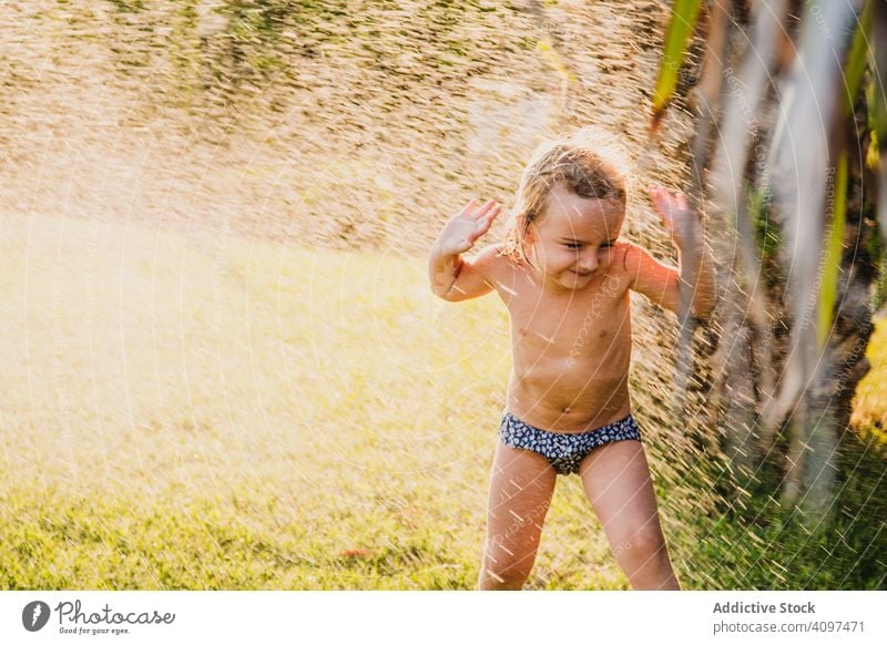 Mädchen ohne Hemd unter spritzendem Wasser im Garten spielen Spray Rasen Sommer sonnig tagsüber Spaß Kind wenig Frauenunterhose Kindheit Glück Freude Hof nass