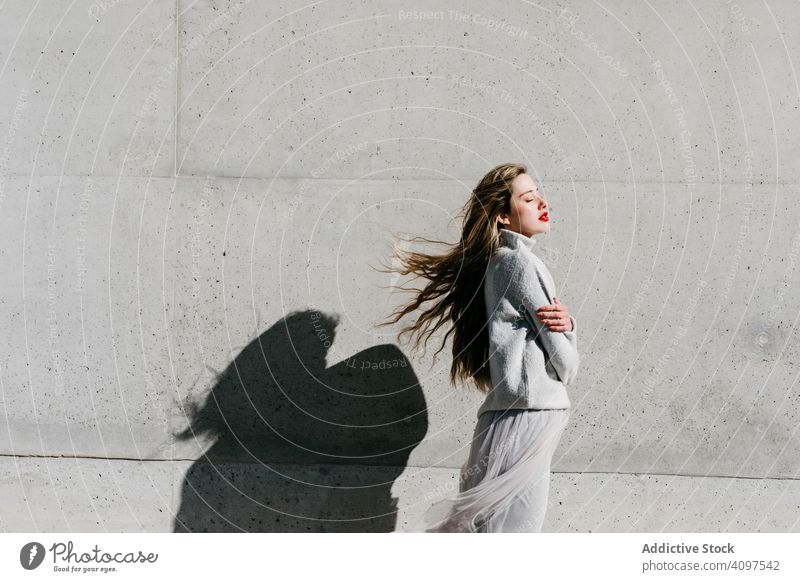 Trendige Dame berührt Haare auf der Straße Frau stylisch sinnlich geschlossene Augen elegant Wand Gebäude Model sonnig tagsüber jung cool urban Outfit zierlich