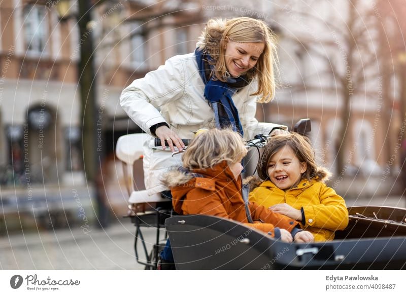 Mutter, die nach ihren Kindern schaut, die im vorderen Teil eines Lastenfahrrads fahren Lastenrad Fahrrad Fahrradfahren Verkehr Dreirad Gesundheit aktiv Zyklus