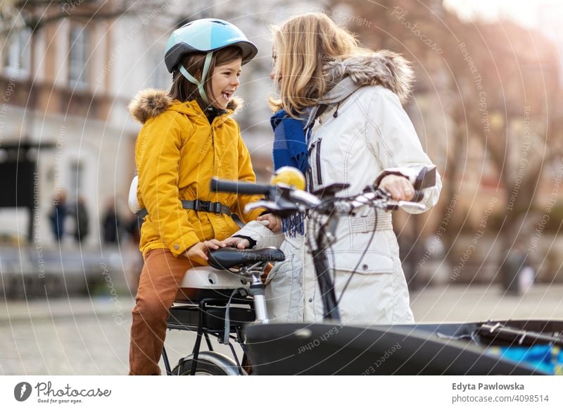 Junge Frau und ihr Sohn fahren mit dem Fahrrad in einer Stadt jung tragend Schutzhelm Fahrradfahren Winter Herbst Mutter Familie Eltern Verwandte Kind Kinder