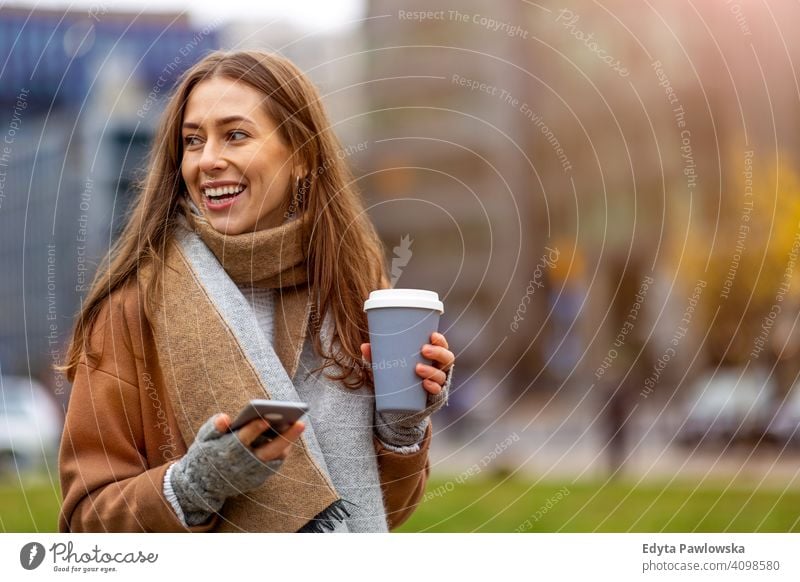 Lächelnde junge Frau mit Smartphone und Kaffeetasse im Freien in städtischer Umgebung Herbst fallen Mädchen schön Wetter Mantel Mode hübsch attraktiv