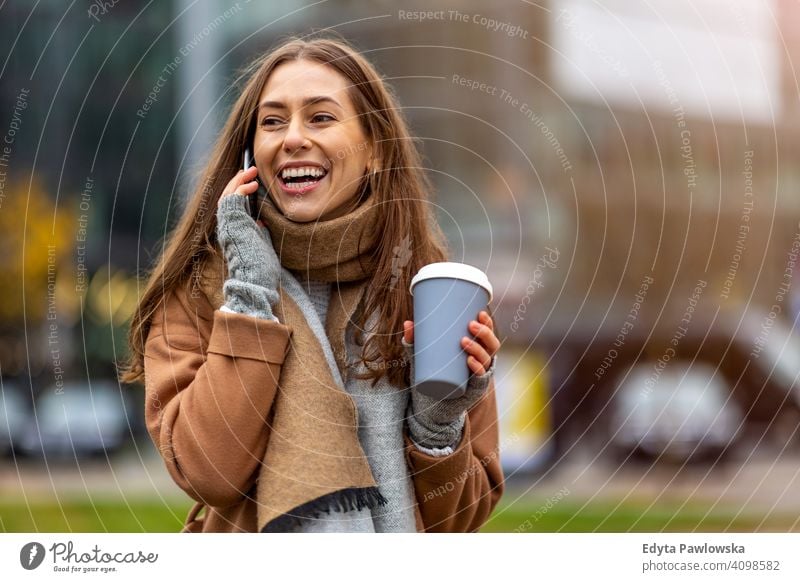 Lächelnde junge Frau mit Smartphone und Kaffeetasse im Freien in städtischer Umgebung Herbst fallen Mädchen schön Wetter Mantel Mode hübsch attraktiv