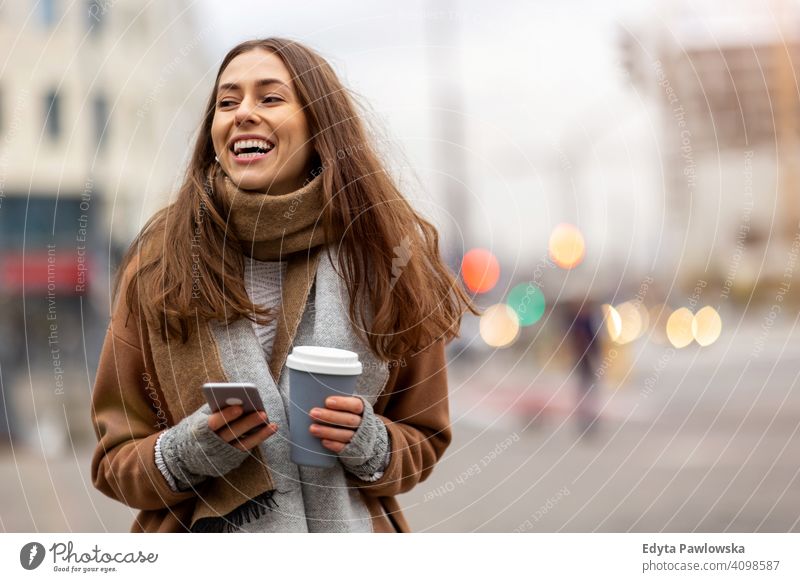 Lächelnde junge Frau mit Smartphone und Kaffeetasse im Freien in städtischer Umgebung Herbst fallen Mädchen schön Wetter Mantel Mode hübsch attraktiv