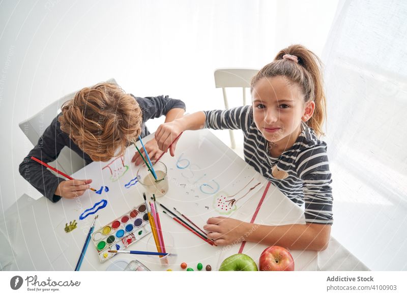 Fokussierte Kinder malen am Tisch Farbe Wasserfarbe Pinselblume fokussiert Freund heimwärts Kunst kreativ Bildung sitzen Zusammensein Mädchen Junge Pigment