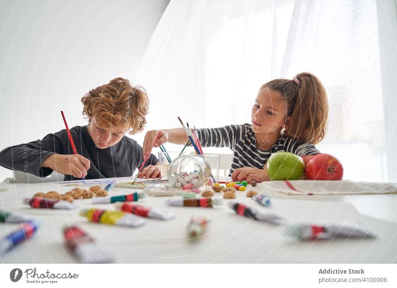 Fokussierte Kinder malen am Tisch Farbe Wasserfarbe Pinselblume fokussiert Freund heimwärts Kunst kreativ Bildung sitzen Zusammensein Mädchen Junge Pigment