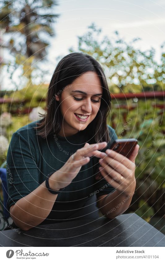 Glückliche Frau mit Smartphone auf der Terrasse benutzend Telefon Lachen Lächeln jung ruhen brünett lässig heiter Sommer blättern Surfen Browsen zuschauend