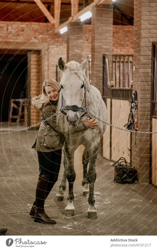 Frau umarmt Pferd mit langer Mähne im Gesicht im Stall Haustier Hengst Tier Pflege apfelgrau Kopf Maul weiß Natur Säugetier Zaumzeug Bauernhof Sattel Feld braun