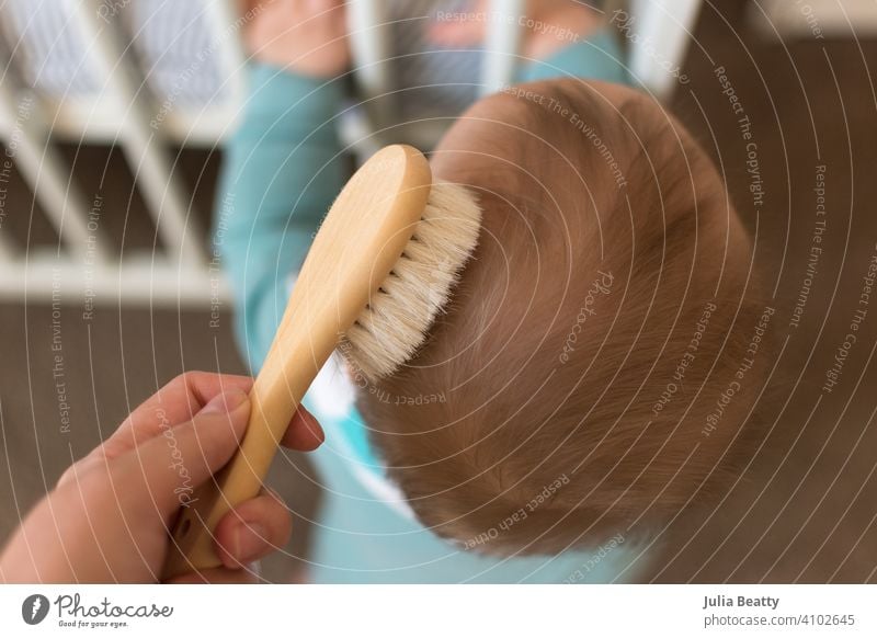 Junges Baby steht auf und hält sich am Gitter fest; die Hand der Mutter bürstet die Haare Behaarung Bürste fein Holz natürlich Borsten Ziegenhaar weich filigran