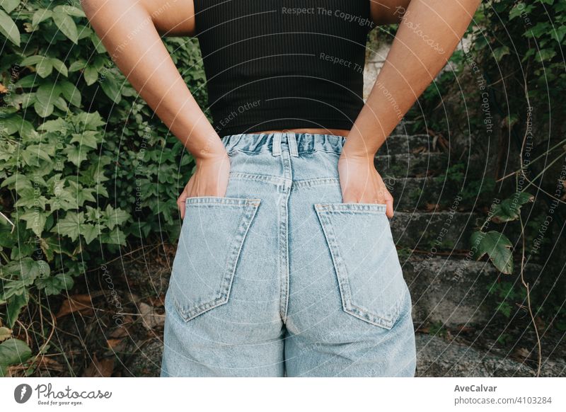 Rückenteil einer Frau, die Mom Jeans trägt, umgeben von Pflanzen und modernem Stil Mama Jeanshose stylisch Taille Menschen Freund Jeansstoff Kleidungsstück hoch