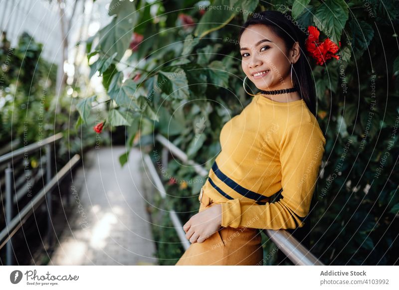 Stilvolle langhaarige asiatische Frau lehnt an einem Zaun im Park mit Blumen Gasse jung Lehnen stylisch Mode Model elegant botanisch trendy Garten Dame modisch