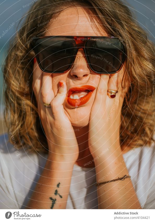 Zeitgenössische ruhende Dame, die ihr Gesicht berührt Frau Sonnenbrille Stil Lippenstift rot modisch Zeitgenosse Hände Handflächen jung Urlaub reisen Frisur