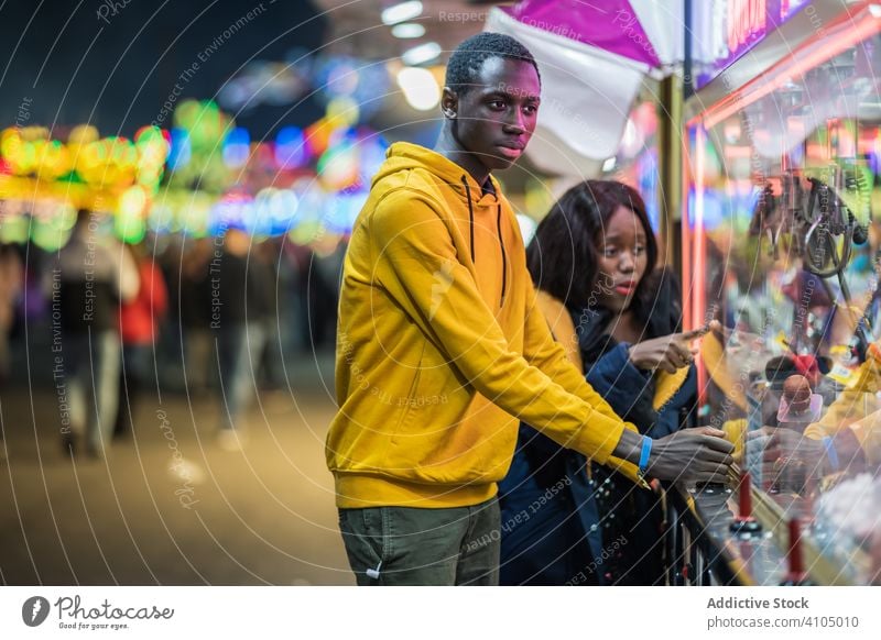 Schwarzer Mann spielt Klauenkran für Freundin Paar Jahrmarkt Arkaden spielen Zusammensein Termin & Datum Abend fangen Spielzeug zuschauen Frau Krallenkran