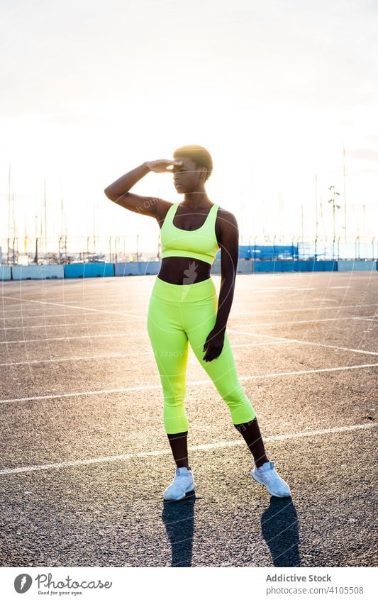 Zuversichtliche ethnische Sportlerin vor dem Training auf dem Sportplatz bei Sonnenuntergang selbstbewusst Motivation Straße Fokus ernst Physis schlank