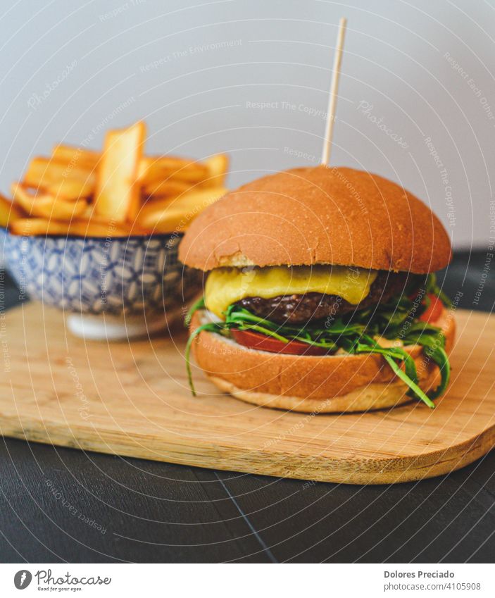 Gourmet-Burger mit Cheddar-Käse und Speck, begleitet von Deluxe-Pommes auf einem Holzbrett Pastetchen Burgerlove Burgerbrötchen glänzend Fleisch