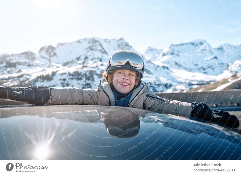 Fröhlicher Junge mit erhobenen Armen aus dem Autofenster Schneeball Winter PKW Lächeln rollen Resort sonnig tagsüber Kind Erholung Lifestyle Glück heiter