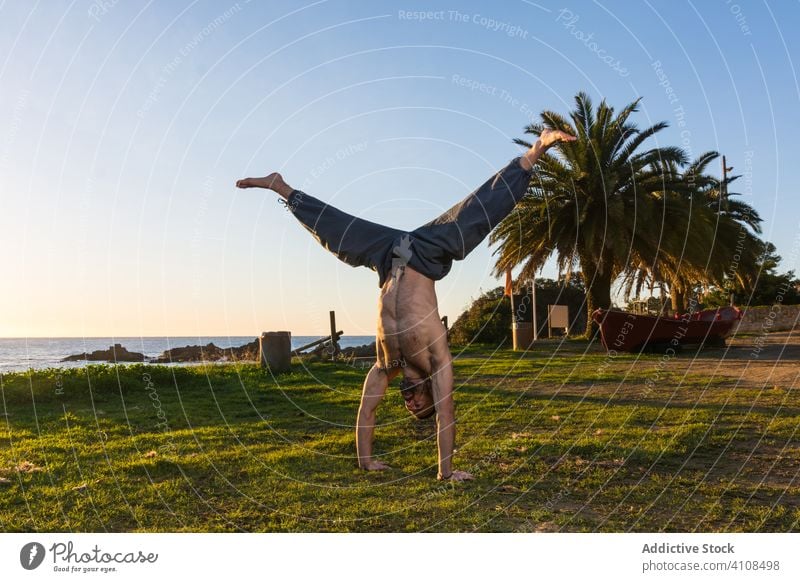 Starker Mann macht Yoga am schönen Strand des Ozeans Körperhaltung Meeresufer Natur Blauer Himmel Handfläche tropisch exotisch Gleichgewicht Dehnung Paradies