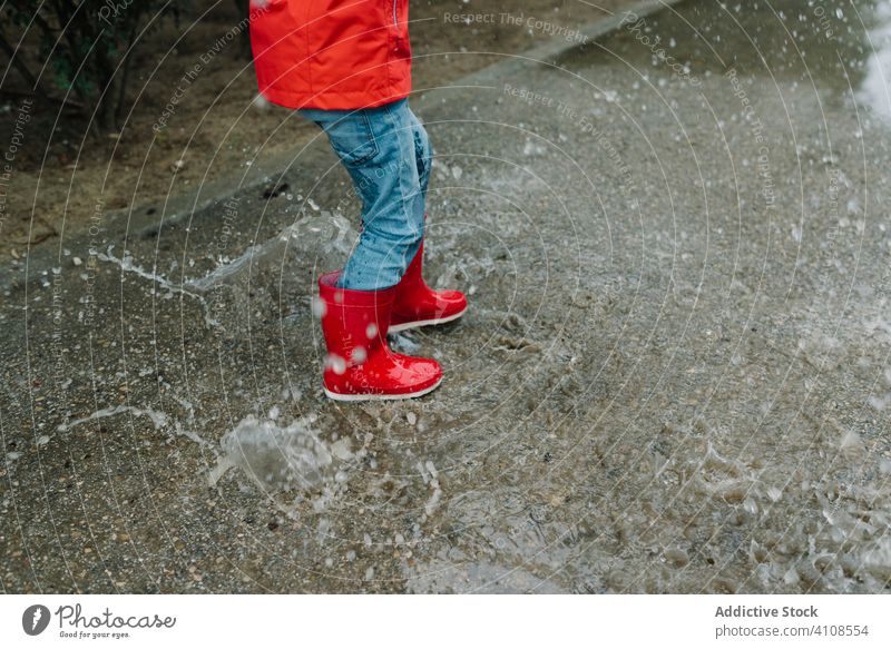 Aktives Kind springt in Pfütze in Parkallee springend unordentlich Saison lustig Wasser nass Schmutz Kindheit Wetter Schlamm Herbst Spiel aktiv Gummistiefel