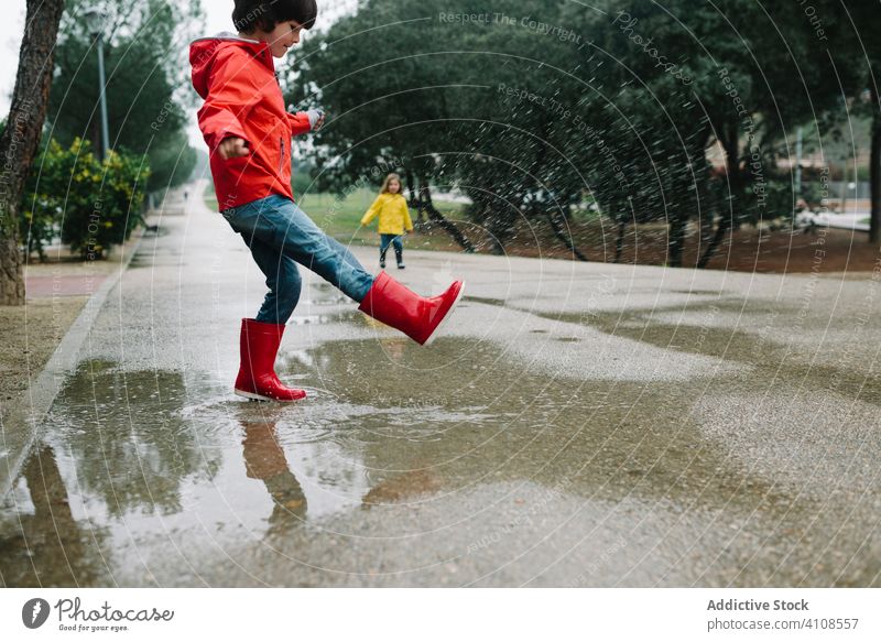 Lustige Kinder spielen in Pfütze im Park Gasse Spielen unordentlich Wetter Zusammensein Geschwister Saison lustig Wasser nass Schmutz Kindheit Schlamm Herbst