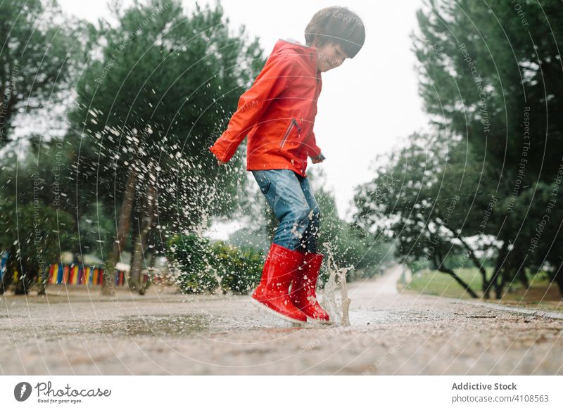 Aktives Kind springt in Pfütze in Parkallee springend unordentlich Saison lustig Wasser nass Schmutz Kindheit Wetter Schlamm Herbst Spiel aktiv Gummistiefel