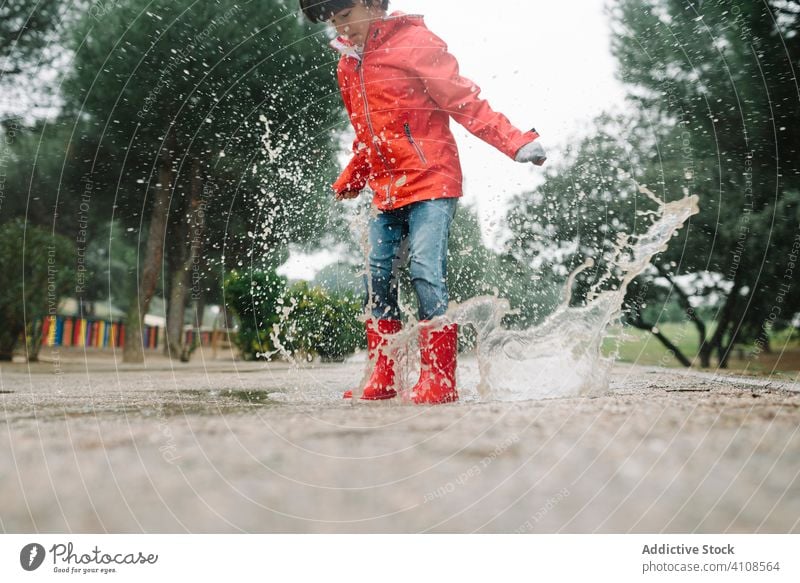 Aktives Kind springt in Pfütze in Parkallee springend unordentlich Saison lustig Wasser nass Schmutz Kindheit Wetter Schlamm Herbst Spiel aktiv Gummistiefel