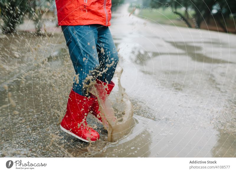 Aktives Kind springt in Pfütze in Parkallee springend unordentlich Saison lustig Wasser nass Schmutz Kindheit Wetter Schlamm Herbst Spiel aktiv Gummistiefel