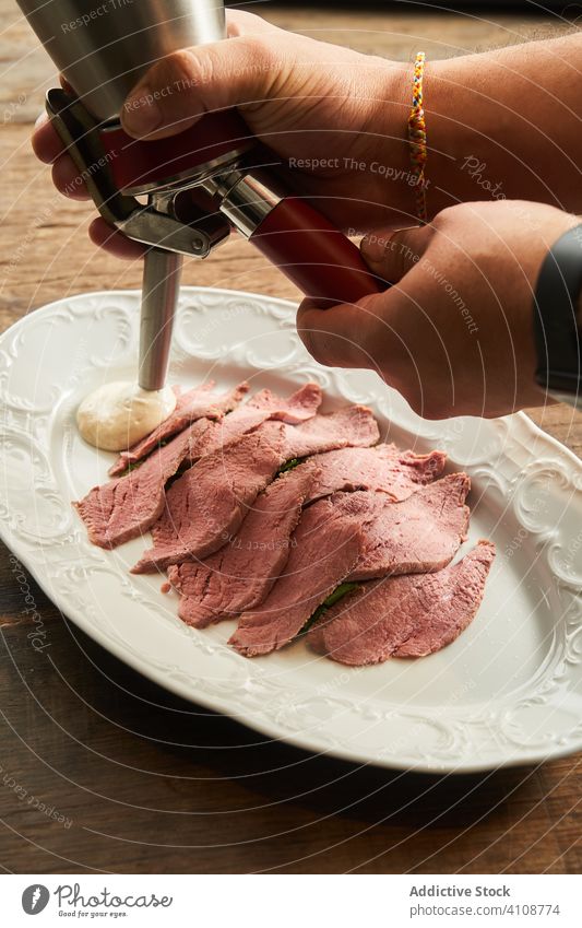 Kropfenkoch gießt Soße in eine Schüssel mit Roastbeef Küchenchef Vanillerostbraten Saucen eingießen Koch Scheibe Steak Teller Speise dienen Lebensmittel