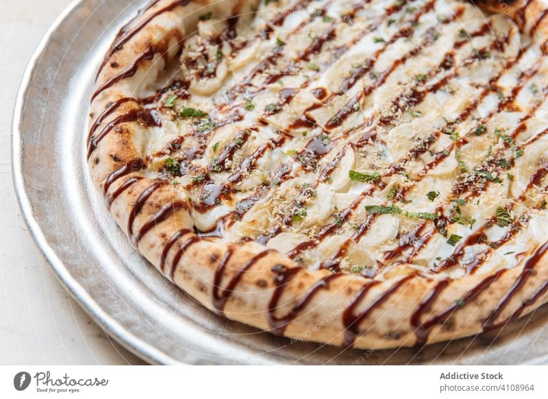 Runde Pizza mit Bananen und Schokoladensauce auf Metalltablett Dessert süß Saucen Nut zerdrückt Minze Belag Zucker Pasteten Konditorei Feinschmecker lecker