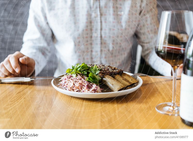 Person, die im Restaurant Rindfleischrippchen am Tisch mit Wein isst Rinderrippen grün Messer Gabel verglast essen trinken Feinschmecker lecker Abendessen