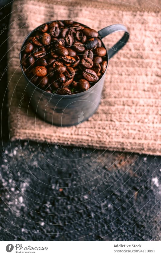 Becher mit Kaffeekörnern auf Serviette Bohne Körner Tisch Braten organisch Bestandteil Energie rustikal unordentlich natürlich Tasse frisch Frühstück braun