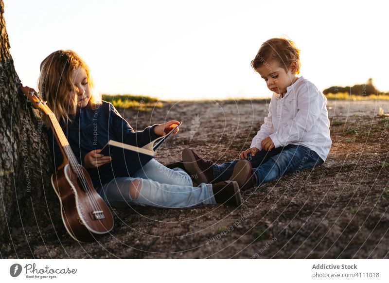 Kinder sitzen unter einem Baum und lesen ein Buch Natur Zusammensein Sommer Ukulele Gitarre ruhen ruhig Schwester Bruder Geschwisterkind Freund Landschaft