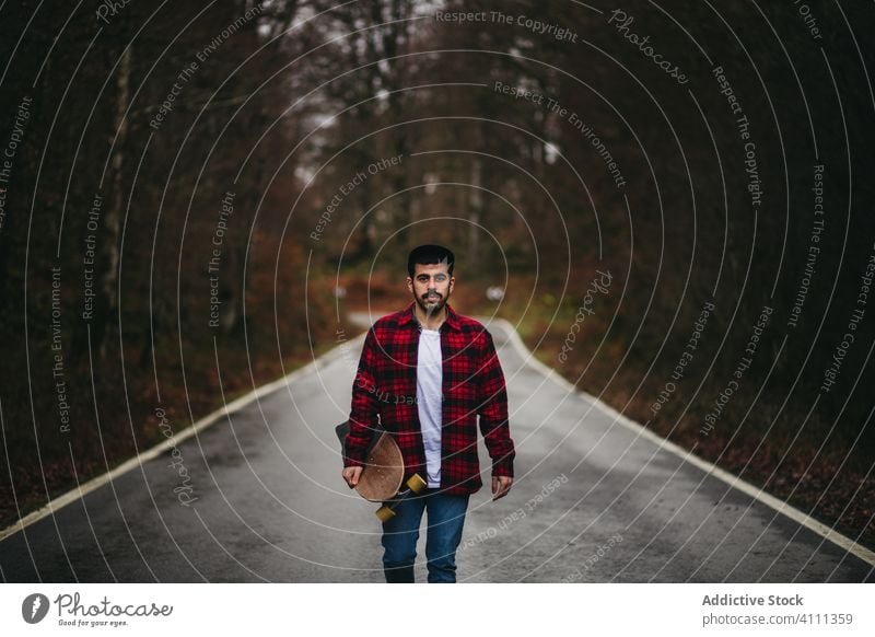 Männlicher Skater auf der Straße im Herbstwald Mann Wald Skateboard Landschaft lässig Spaziergang Stil männlich Baum leer Asphalt Natur Freiheit Abenteuer