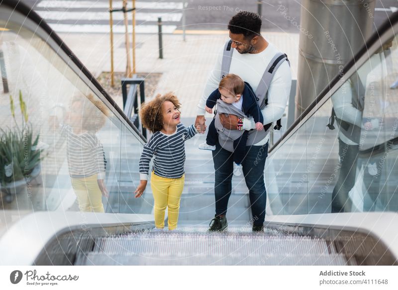 Ethnischer Vater mit Kindern auf Rolltreppe Mann Zusammensein Tochter Sohn Glück urban Großstadt trendy Liebe Partnerschaft männlich lässig Treppe modern