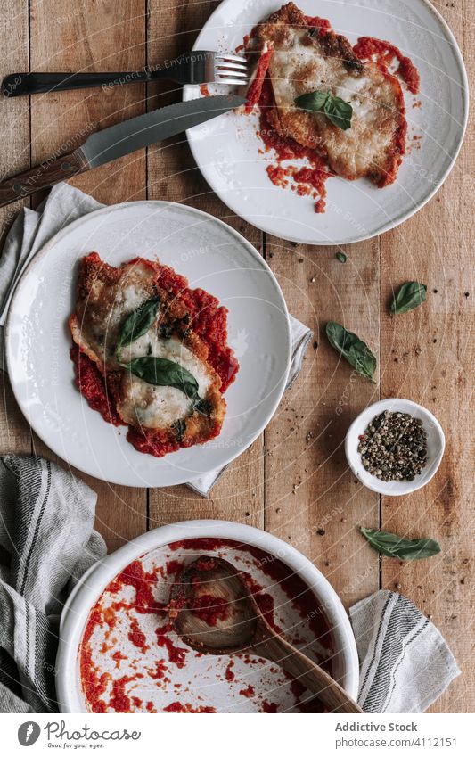 Schmackhaftes Hähnchen mit Parmesan und Basilikum in Tomatensauce gebraten Braten Saucen Käse Tisch rustikal Utensil Serviette Gewürz Teller Schalen & Schüsseln