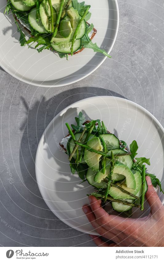 Person mit Toast und grünem Gemüse Zuprosten Gesundheit Vegetarier natürlich frisch Kraut Lebensmittel Hand Brot Belegtes Brot Avocado Salatgurke Mahlzeit