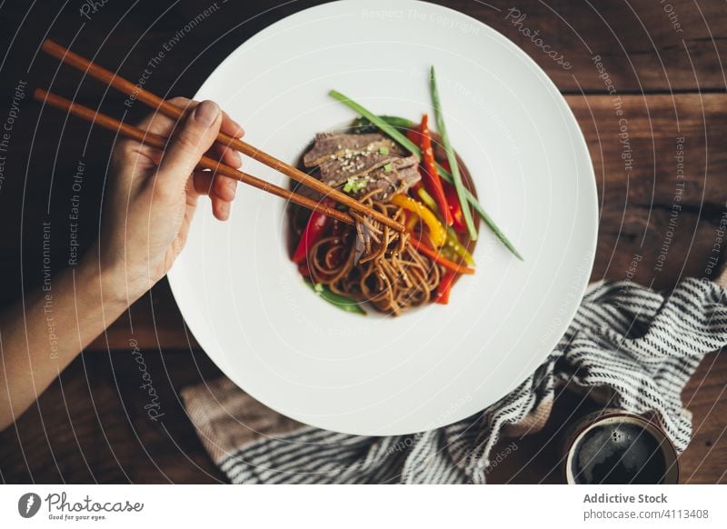 Person, die asiatische Nudeln mit Stäbchen isst Lebensmittel Speise Essstäbchen essen Hand Fleisch Gemüse Tradition Mahlzeit lecker hölzern weiß Teller